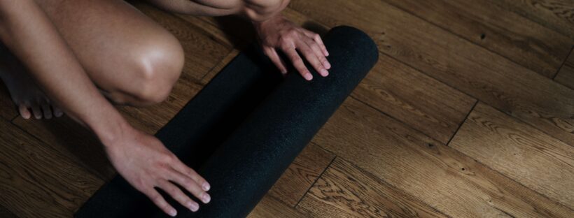 Man sieht die Knie und Hände einer Frau, die gerade eine Yogamatte ausrollt